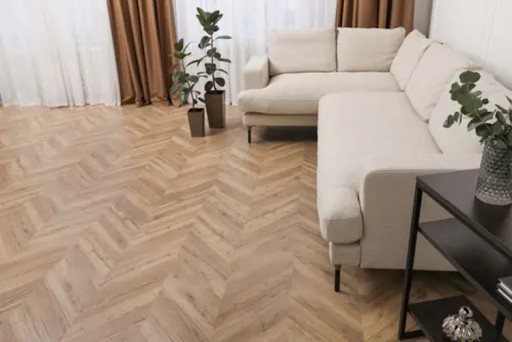 A bright living room with a cream sectional sofa, potted plants, and light wood herringbone flooring.