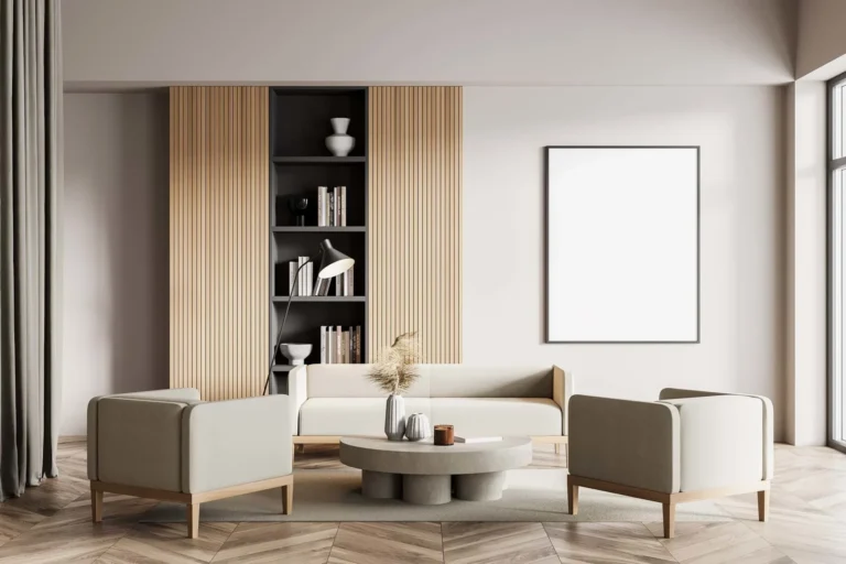 Modern, minimalist living room featuring cream-colored seating, a round concrete coffee table, chevron wood flooring, and a large blank framed canvas on the wall next to a wooden slatted bookshelf.