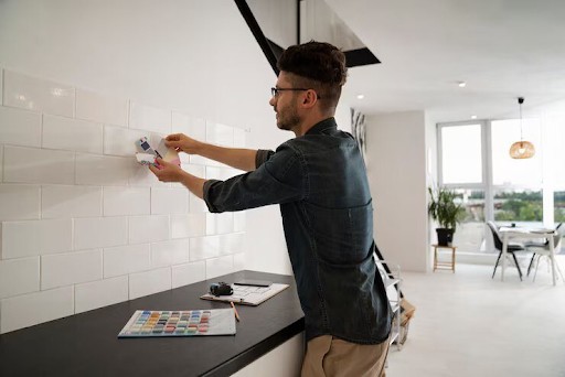 Man holding tile samples against a white tile wall.