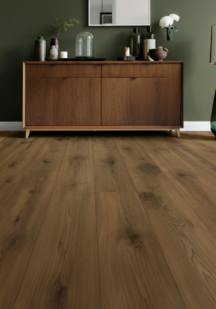 Dark brown wood plank flooring in a room with a wooden credenza and green wall.